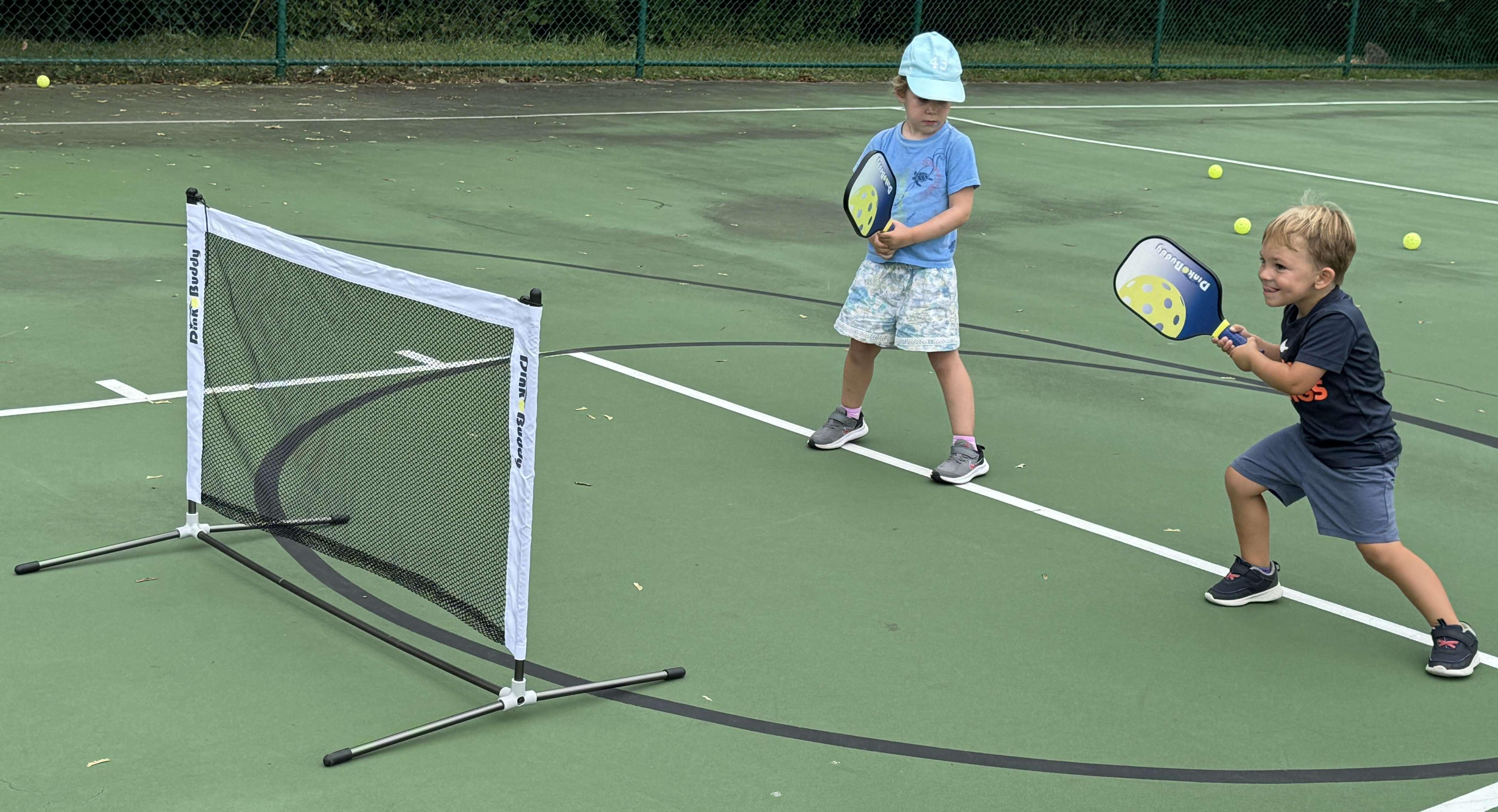 Young boy and girl playing pickleball on outdoor court with paddles and net